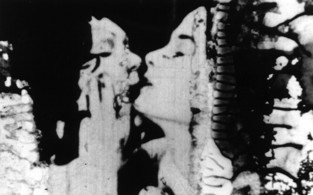 Filmstill aus THE COLOR OF LOVE: Ein sich küssendes Paar. An den Rändern zersetzt sich der Filmstreifen.