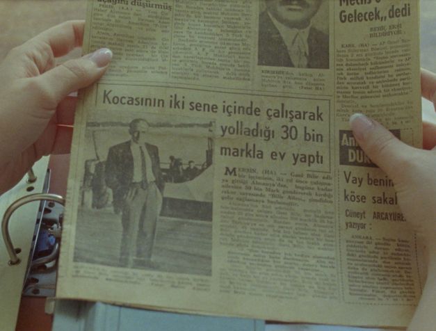 Filmstill aus dem Film „Zwischenwelt“ von Cana Bilir-Meier. Zwei Hände halten eine vergilbte türkischsprachige Zeitung über einem Aktenordner.