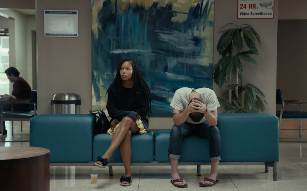 Filmstill aus TEST PATTERN: Ein junges Paar sitzt nebeneinander in einem Wartezimmer auf einem blauen Sofa.