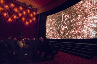 Publikum im Kino schaut auf die Leinwand, auf der der Trailer der Berlinale zu sehen ist.