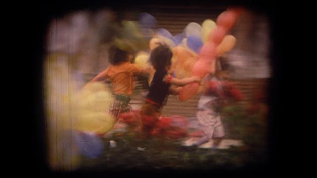 Filmstill aus dem Film "Majmouan" von Mohammadreza Farzad. Mehrere Kinder rennen mit bunten Luftballons in der Hand über eine Wiese