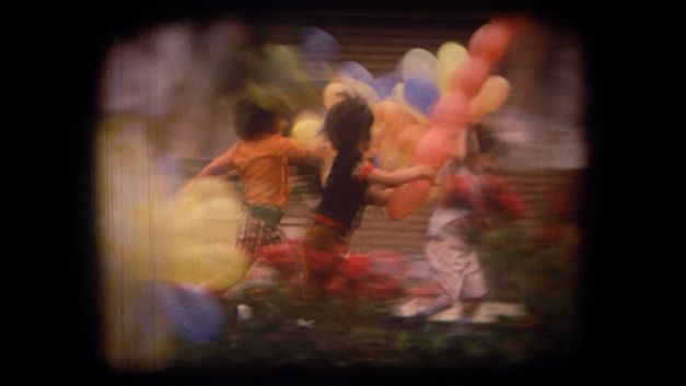 Still from the film "Majmouan" by Mohammadreza Farzad. Several children run across a meadow with colorful balloons in their hands