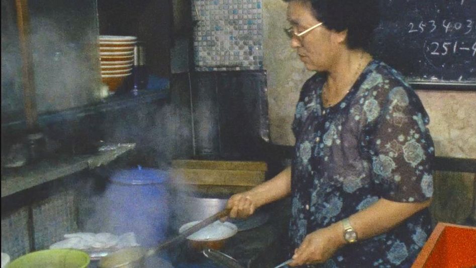 Film still from THE OTHER HIROSHIMA: A woman works at the stove in a small kitchen.