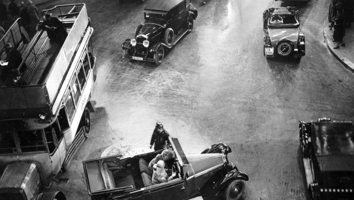 Filmstill aus ASPHALT: Eine Berliner Straßenszene aus den 1920er Jahren. Man sieht eine Kreuzung mit Autos und Bussen, in der Mitte steht ein Polizist.