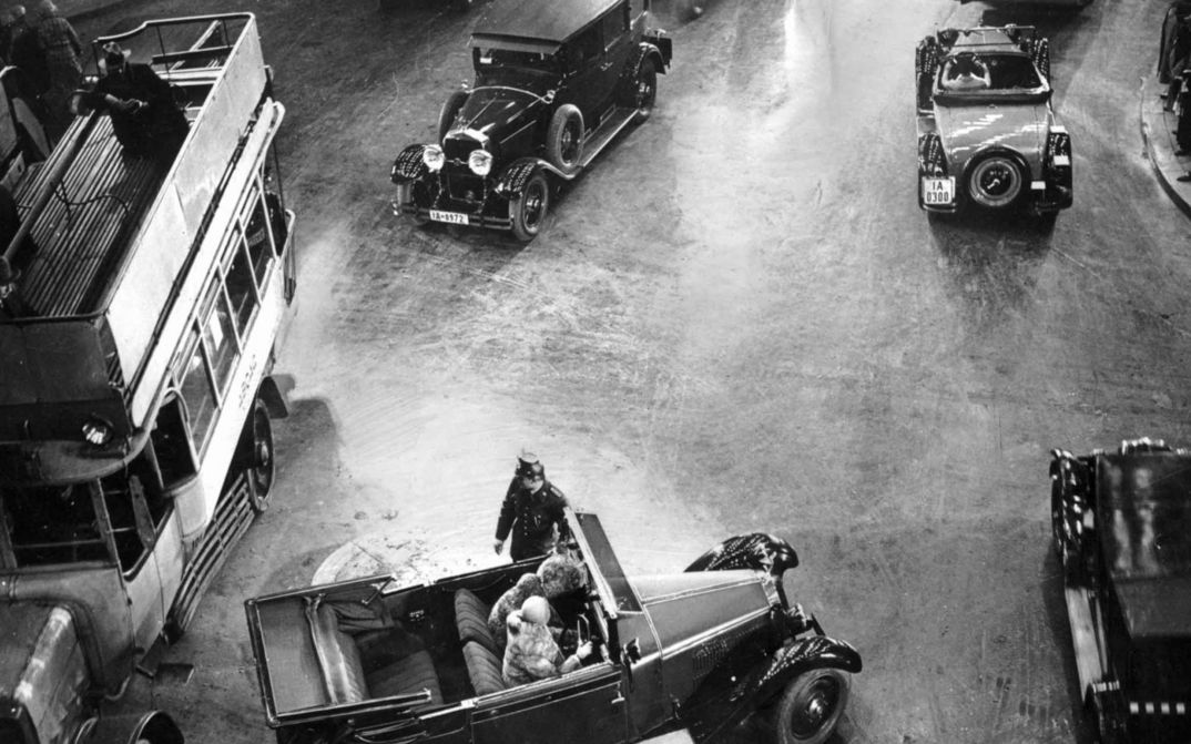 Film still from ASPHALT: A street scene in Berlin from the 1920s. You can see an intersection with cars and buses, and a police officer standing in the middle.