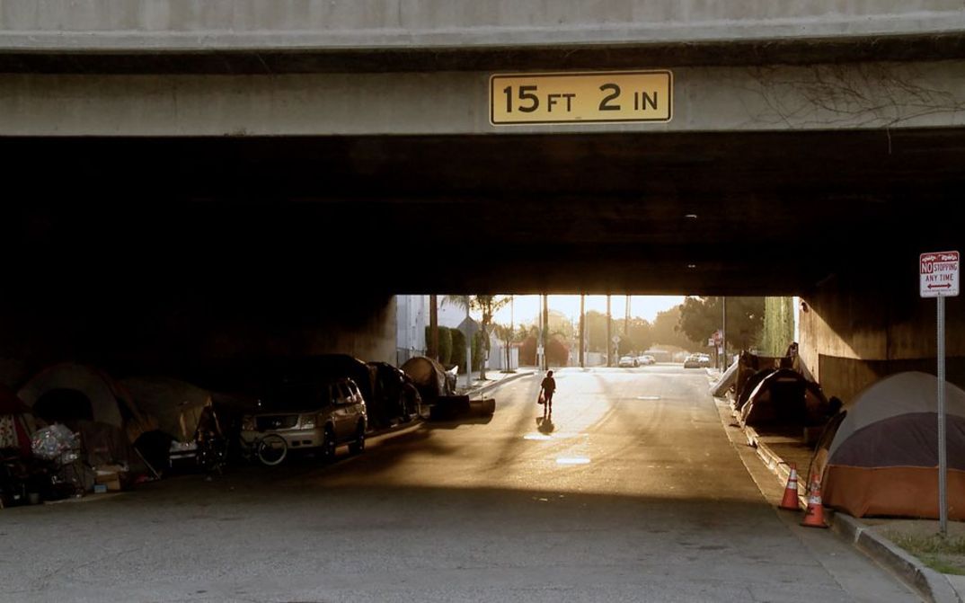 Still aus James Bennings „The United States of America“: Wir schauen durch eine Straßenunterführung. Auf der anderen Seite scheint die Nachmittagssonne. Unter der Brücke am Straßenrand Zelte, in denen Menschen leben.