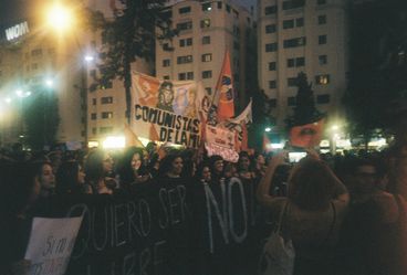 35mm colour photo of a protest in the evening. A group of women march banners and signs.