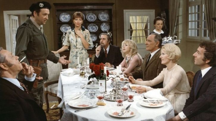 Film still from LE CHARME DISCRET DE LA BOURGEOISIE: A group of elegantly dressed people are sitting around a dining table.