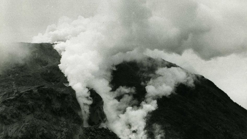 Filmstill aus LA SOUFRIÈRE: In einer schwarz-weißen Aufnahme strömt Rauch aus einem Vulkan.