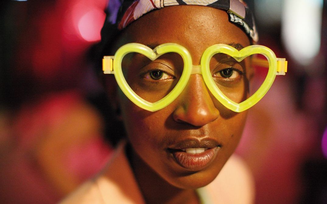 Filmstill aus RAFIKI: Eine junge Frau mit einer neongelben Brille in Herzform blickt direkt in die Kamera.