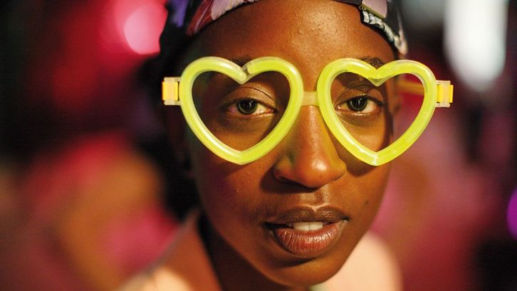 Filmstill aus RAFIKI: Eine junge Frau mit einer neongelben Brille in Herzform blickt direkt in die Kamera.