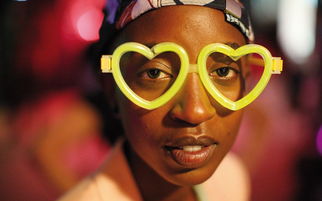 Filmstill aus RAFIKI: Eine junge Frau mit einer neongelben Brille in Herzform blickt direkt in die Kamera.