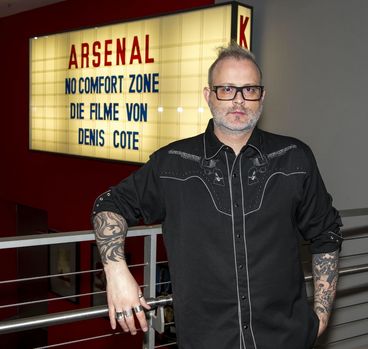 Denis Cote vor Leuchtkasten mit seinem Namen 