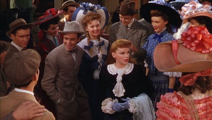 Filmstill aus MEET ME IN ST. LOUIS: Man sieht eine Gruppe von Menschen in historischen Kostümen um 1900, in der Mitte steht Judy Garland.