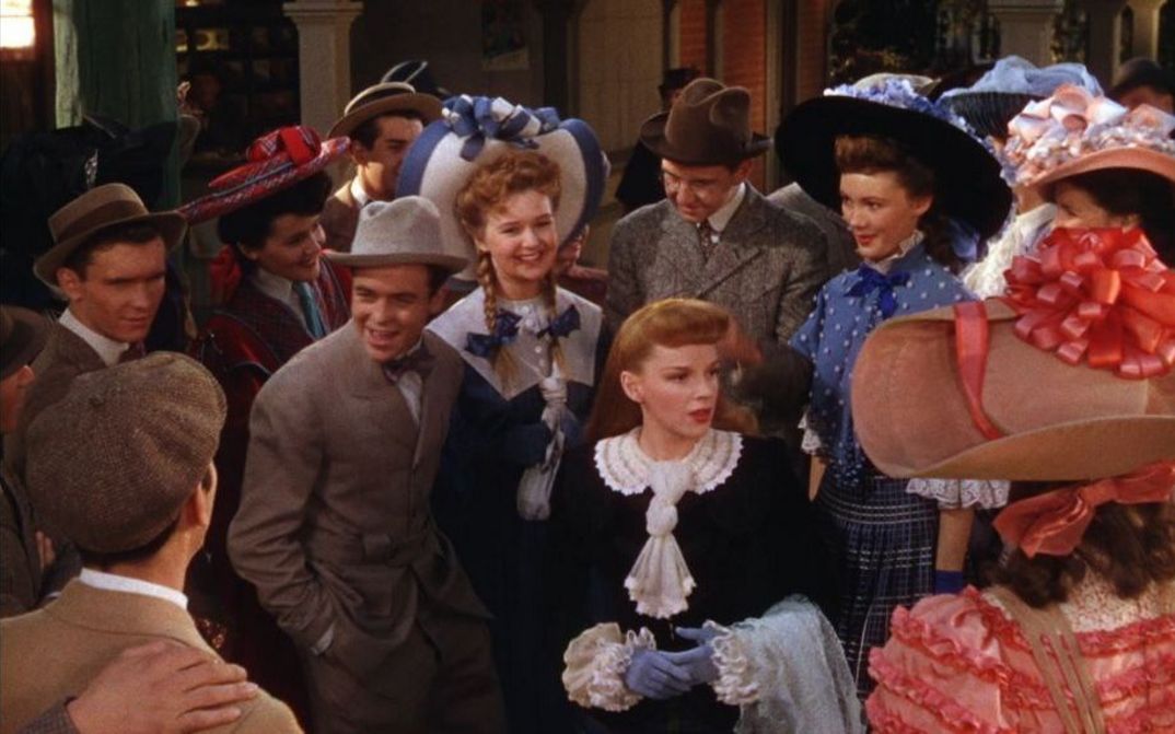 Filmstill aus MEET ME IN ST. LOUIS: Man sieht eine Gruppe von Menschen in historischen Kostümen um 1900, in der Mitte steht Judy Garland.