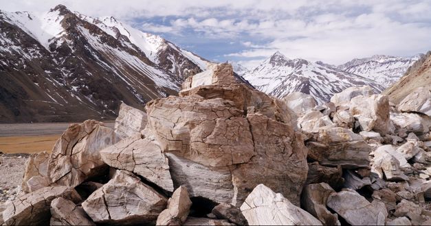 Filmstill aus THE CORDILLERA OF DREAMS: Ein rissiger Gesteinshaufen. Im Hintergrund teils schneebedeckte Berge.