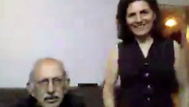 Film still from "Was hast du gestern geträumt, Parajanov?" by Faraz Fesharaki. It shows a blurred close-up of an older man sitting and a woman standing to his right. They are looking towards the camera.