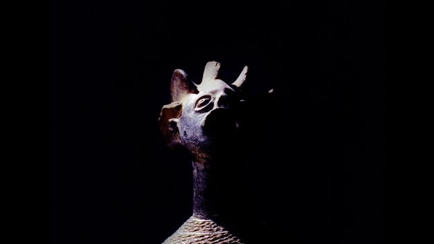Filmstill aus dem Film "Under the White Mask: The Film That Haesaerts Could Have Made" von Matthias De Groof. Man sieht eine Holzmaske vor einem schwarzen Hintergrund.