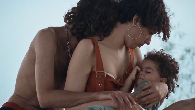 Eine Frau hält ein schlafendes Kleinkind im Arm, während eine weitere Person hinter ihr steht.