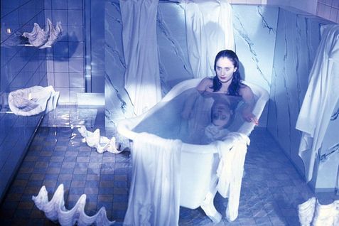 Junge Frau sitzt in einer Badewanne in einem blau beleuchteten Badezimmer.