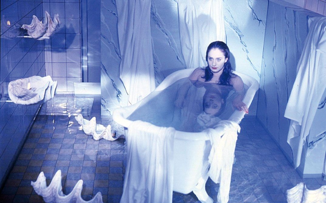 Junge Frau sitzt in einer Badewanne in einem blau beleuchteten Badezimmer.