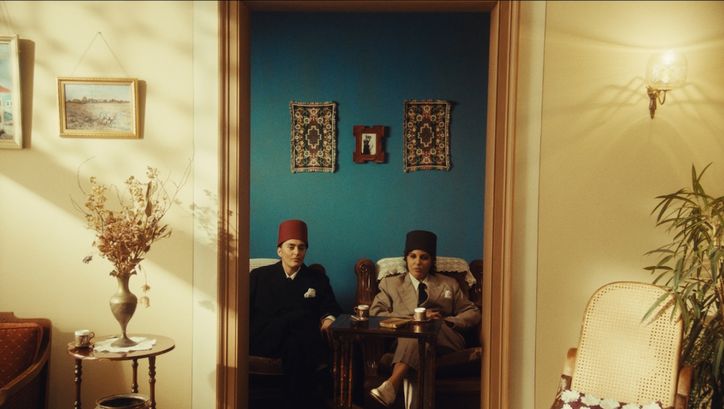 Film still from NEO NAHDA: Two women dressed as men sit between a door frame and look directly into the camera.