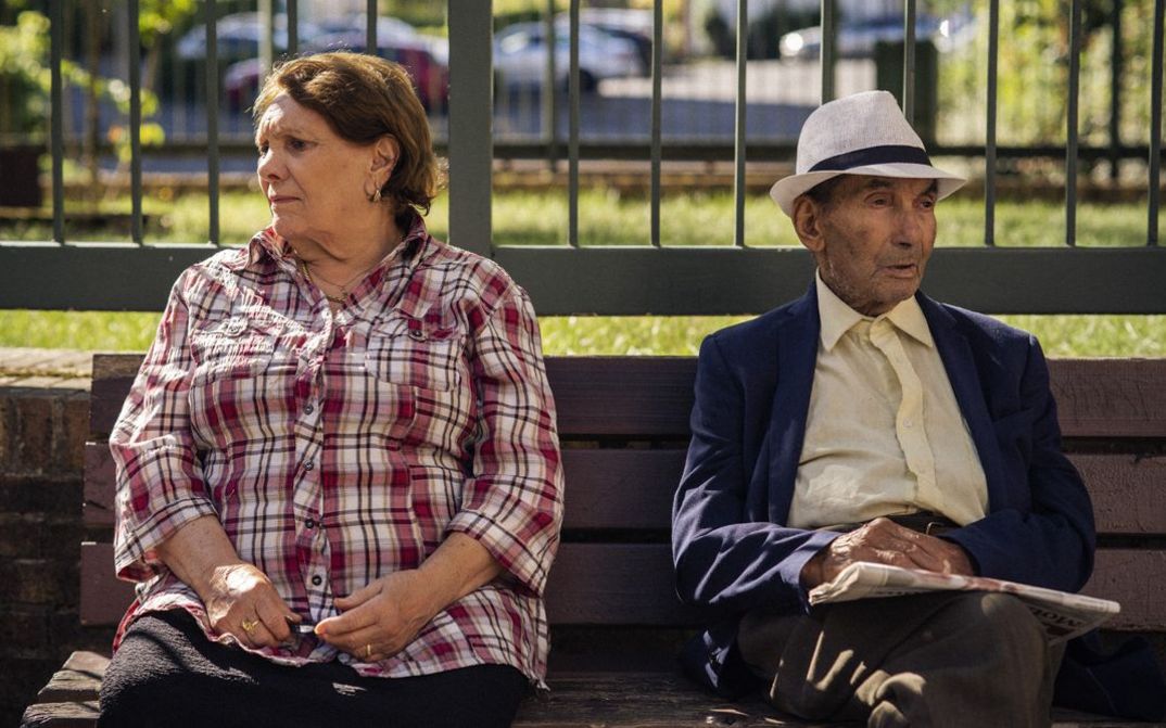 Filmstill aus THEIR ALGERIA. Ein älteres Paar sitzt auf einer Parkbank, sie blicken in entgegengesetzte Richtungen.