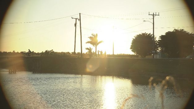Silhouetten von Leuten am Wasser bei Sonnenuntergang, Spiegelungen sichtbar.