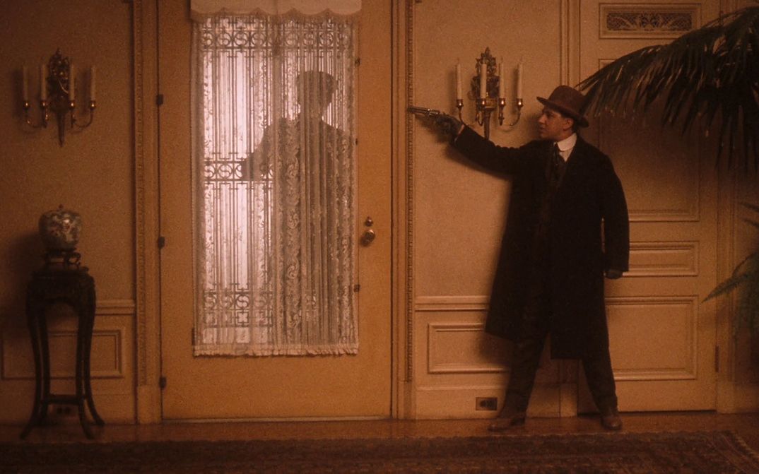 Filmstill aus THE GODFATHER PART II: Ein Mann wartet in einem Haus hinter der Tür mit gezogener Pistole.