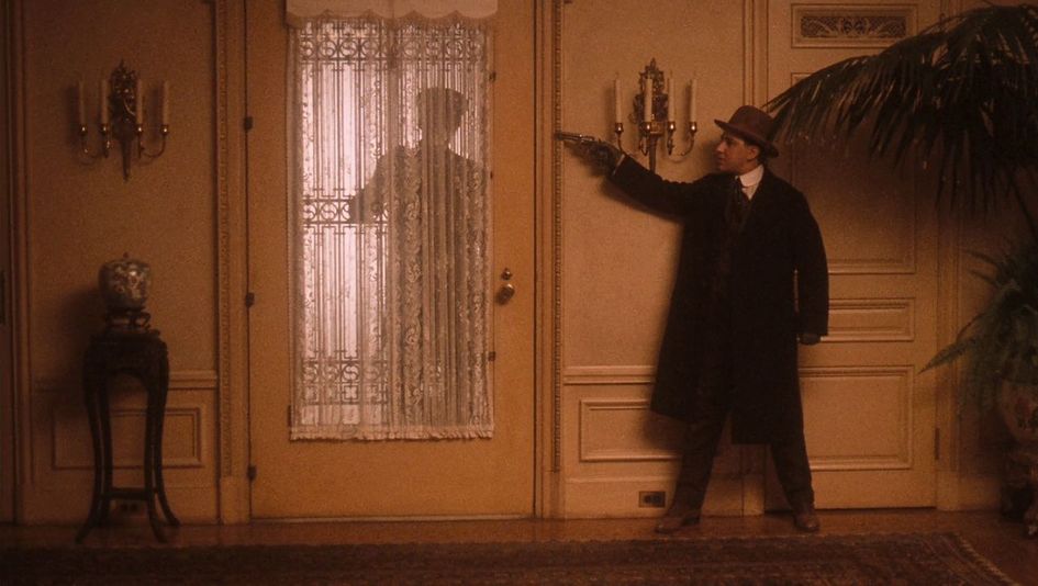 Film still from THE GODFATHER PART II: A man waits in a house behind the door with his gun drawn.