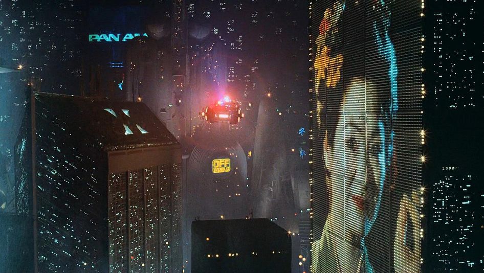 Filmstill aus BLADE RUNNER: Eine futuristische Szenerie mit beleuchteten Hochhäusern und Flugobjekten.