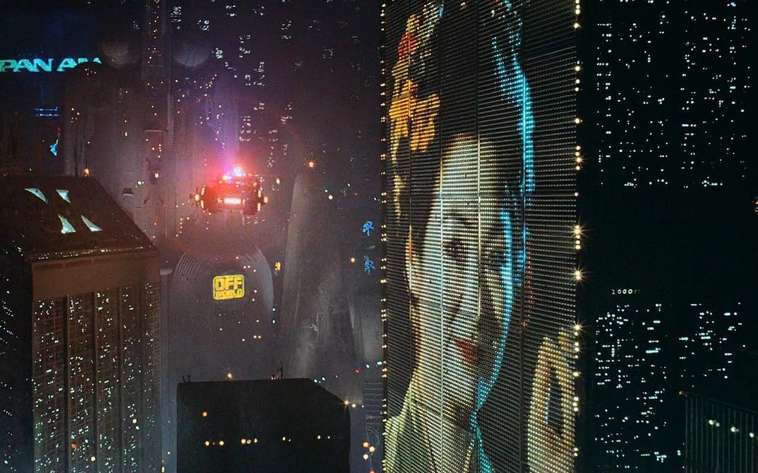 Filmstill aus BLADE RUNNER: Eine futuristische Szenerie mit beleuchteten Hochhäusern und Flugobjekten.