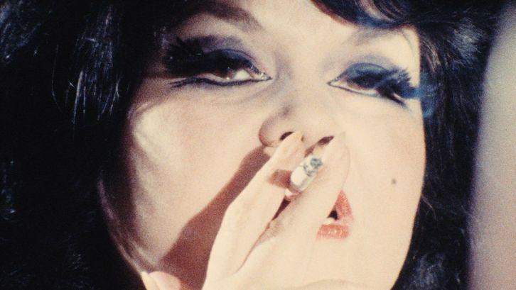 Film still from TALLY BROWN, NEW YORK: Close-up of a dark-haired woman with dark eye make-up smoking a cigarette.