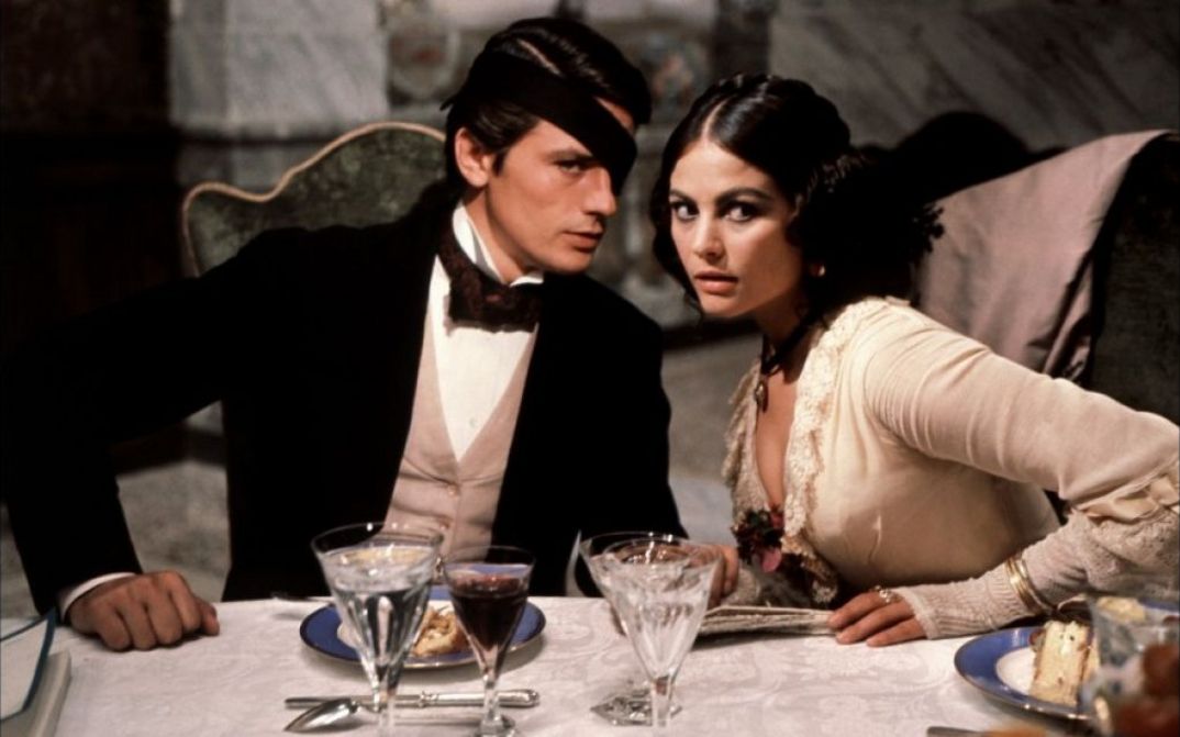 Filmstill aus IL GATTOPARDO: Ein elegant gekleidetes Paar sitzt an einem feierlich gedeckten Tisch.