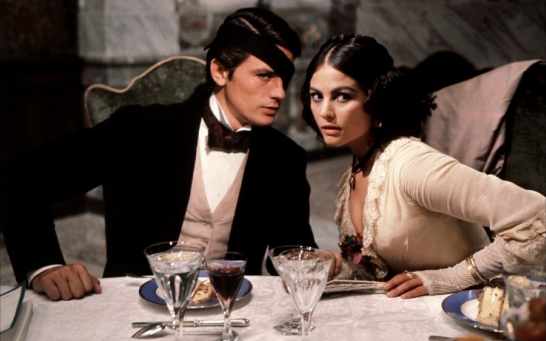 Filmstill aus IL GATTOPARDO: Ein elegant gekleidetes Paar sitzt an einem feierlich gedeckten Tisch.