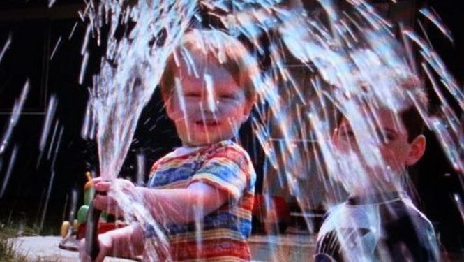 Filmstill aus IN OUR WATER: Ein Kind spielt mit einem Wasserschlauch.