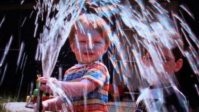 Film still from IN OUR WATER: A child plays with a water hose.