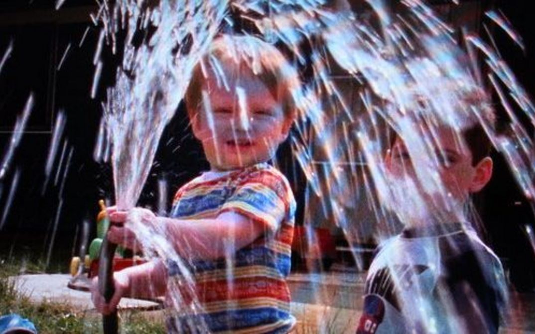 Filmstill aus IN OUR WATER: Ein Kind spielt mit einem Wasserschlauch.
