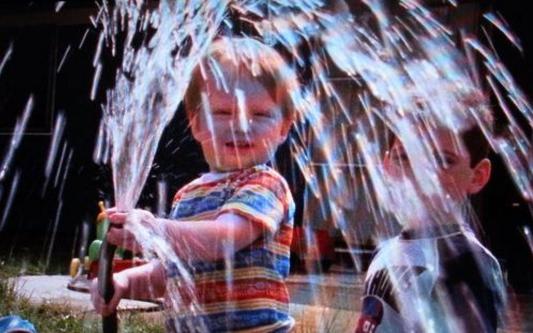 Film still from IN OUR WATER: A child plays with a water hose.