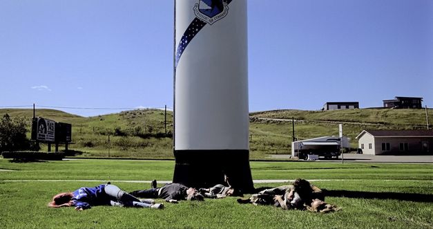 Still from the film "Nuclear Family" by Erin Wilkerson and Travis Wilkerson. Family members lay down on the grass in front of a large vertical missile.