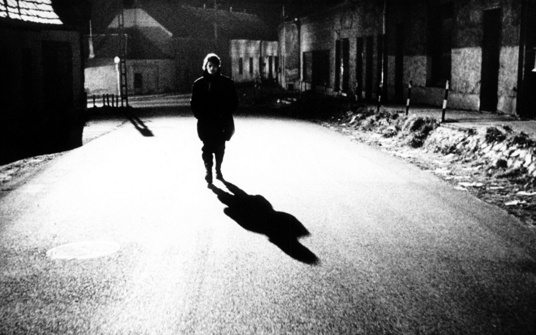 Film still from Werckmeister Harmóniák: A person is walking alone down a street at night. A streetlight casts a shadow.