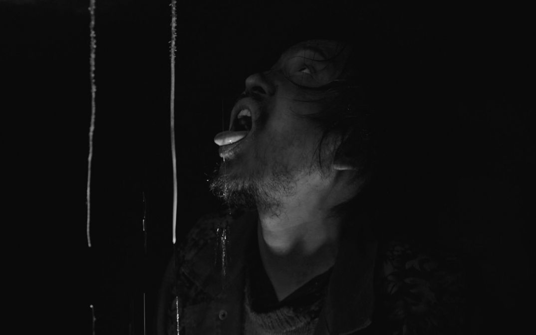 Black-and-white image of a man with open mouth, water dripping in darkness.
