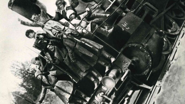 Filmstill aus ARSENAL: Mehrere Männer mit Gewehren stehen auf einer Lokomotive. Das Bild ist nach links gekippt.