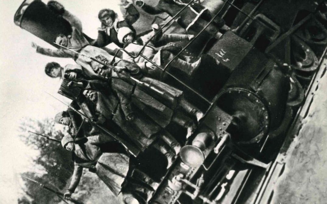 Film still from ARSENAL: Several men with rifles are standing on a locomotive. The picture is tilted to the left.