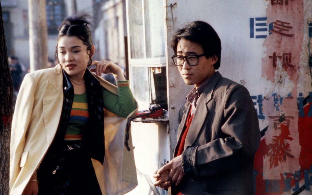 Filmstill aus XIAO WU: Ein Mann und einer Frau stehen an einer Straßenecke. Auf einer Hauswand sind chinesische Schriftzeichen zu sehen.
