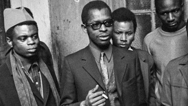 Filmstill aus MES VOISINS: Vier Männer, teils in Anzügen, Schals, Kopfbedeckung oder Brille oder am Rauchen.