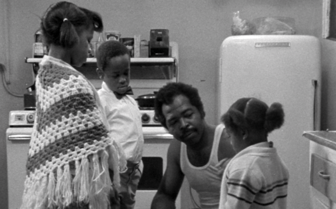 Filmstill aus BLESS THEIR LITTLE HEARTS: Ein Mann sitzt mit seinen drei Kindern in der Küche.