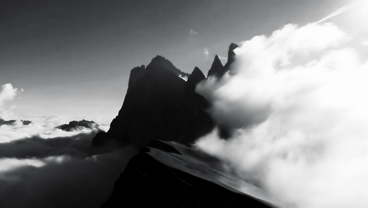 Film still from LA NATURE: The silhouettes of mountain peaks rise out of a cloud cover. On the left is a large cloud.