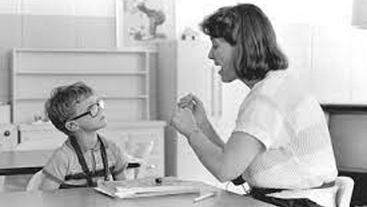 Film still from DEAF. A teacher and a child are sitting at a table in the classroom.