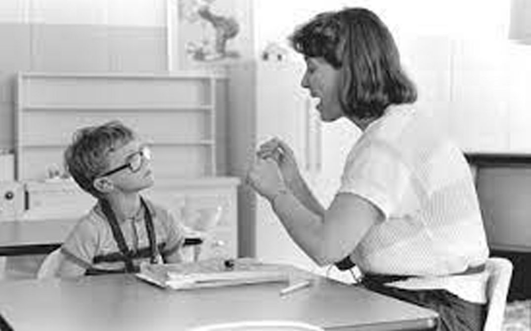 Film still from DEAF. A teacher and a child are sitting at a table in the classroom.